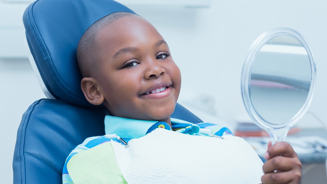 Smiling boy in dental chair with mirror